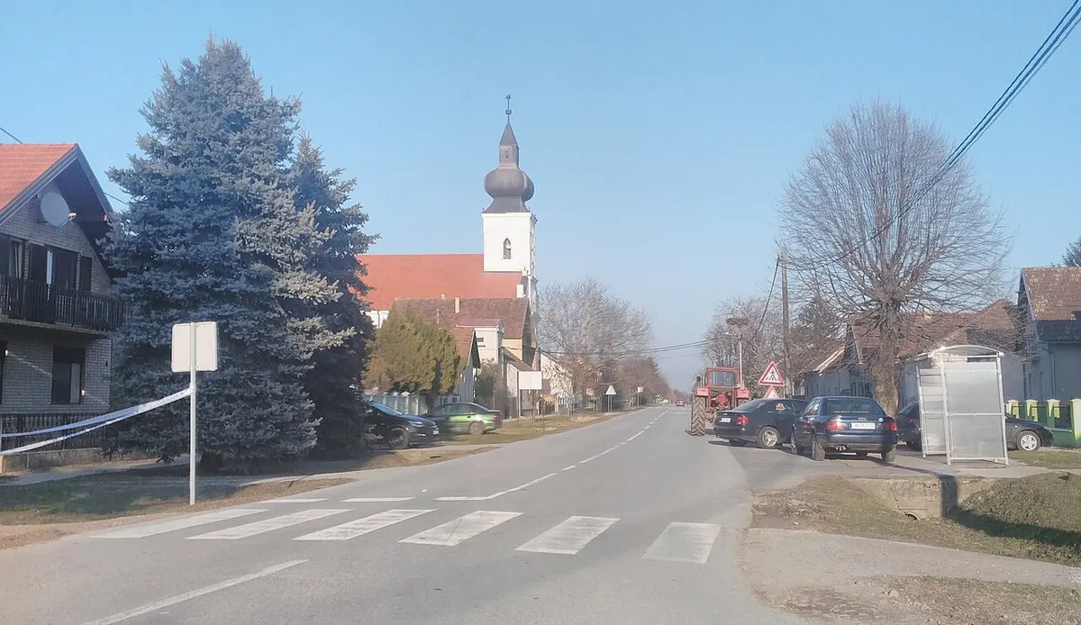 Ulica u Korođu s kućama, drvećem i crkvenim tornjem u daljini